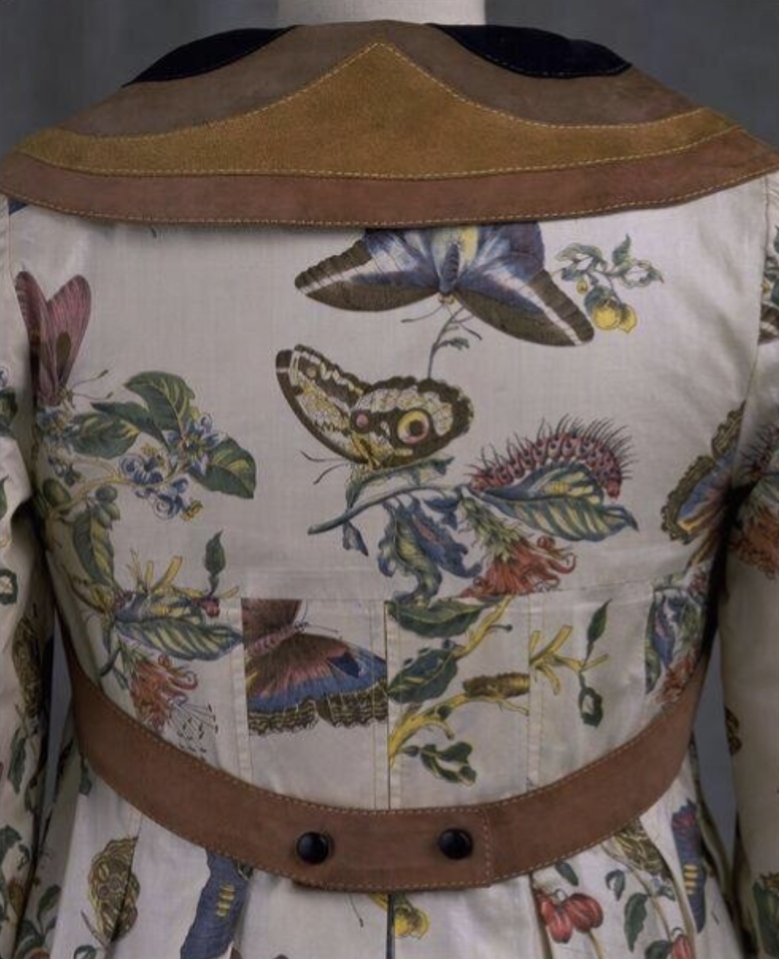 Close-up of a 1971 butterfly-print jacket possibly designed by Bill Gibb for Baccarat, featuring glazed cotton fabric with botanical motifs and suede lapels resembling butterfly wings.